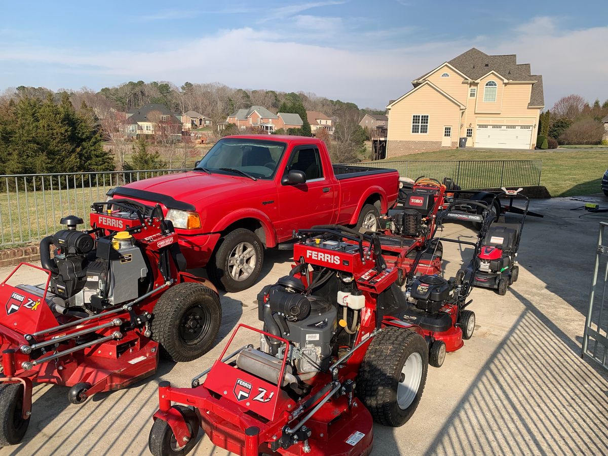 A red Ford Ranger parked behind a fleet of red Ferris stand‑on mowers and a Toro on a concrete pad