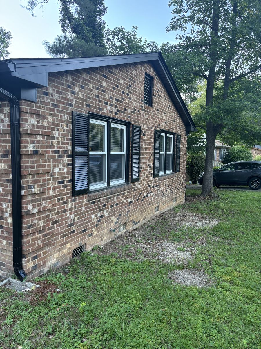 Brick ranch house with black trim and bare, weedy foundation beds